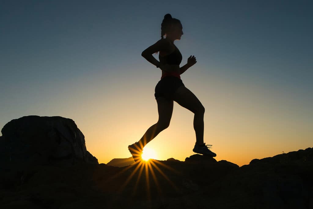 woman trail runner in the mountains at sunset