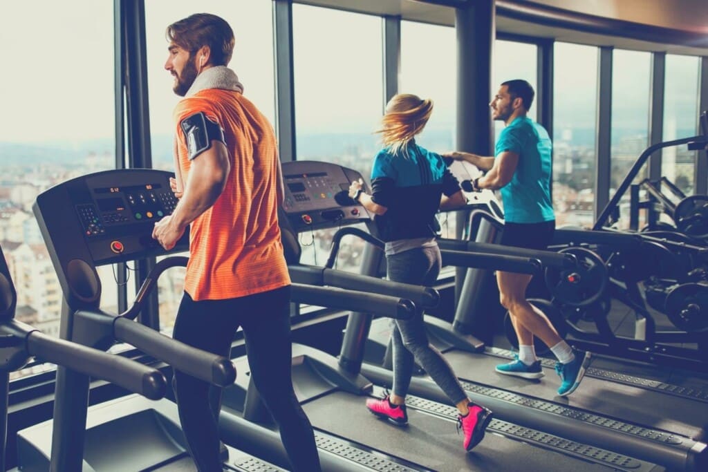male and female runners on treadmill in an indoor gym with personal trainer