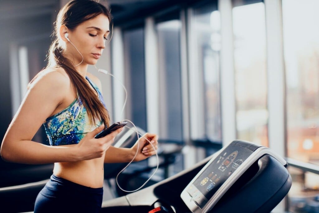 woman looking at her phone while running on a treadmill
