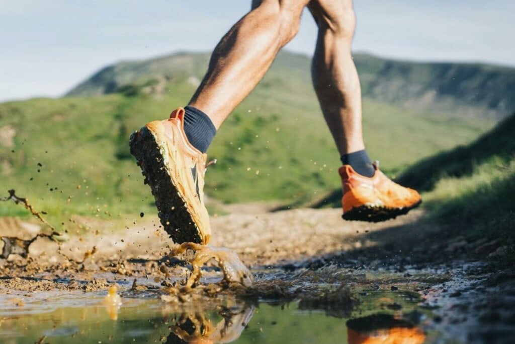 a man running on a muddy trail wearing Altra Olympus 5