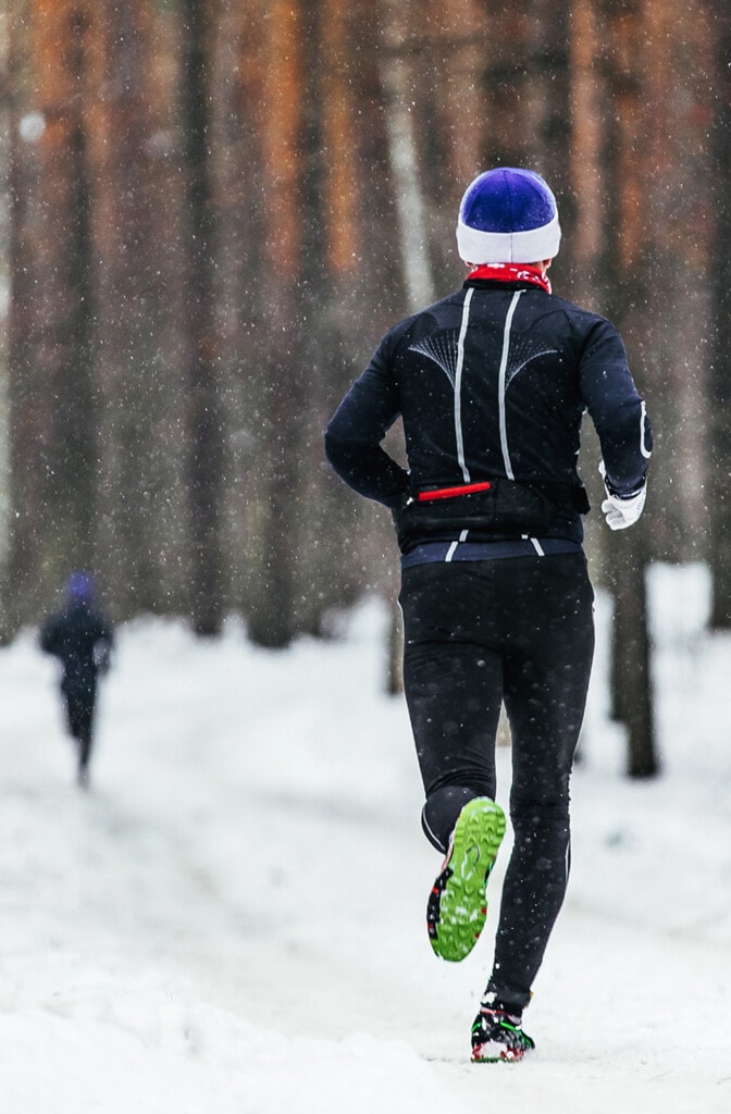 male athlete runner running in falling snow in forest